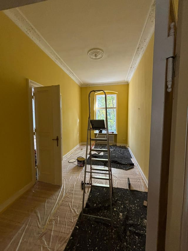 Painter's ladder and dust sheets in a mustard-yellow hallway during decorating work